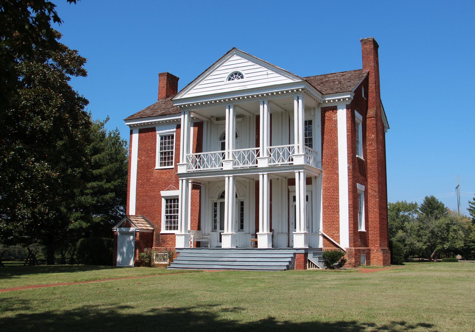 Two-story red-brick house with a white columned double porch under a blue sky.